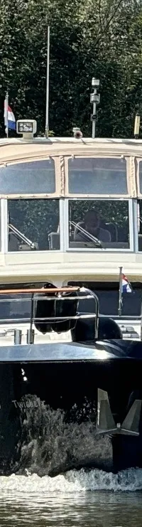 Een donkerblauwe motorboot met een lichte opbouw vaart op een waterweg met bomen op de achtergrond.