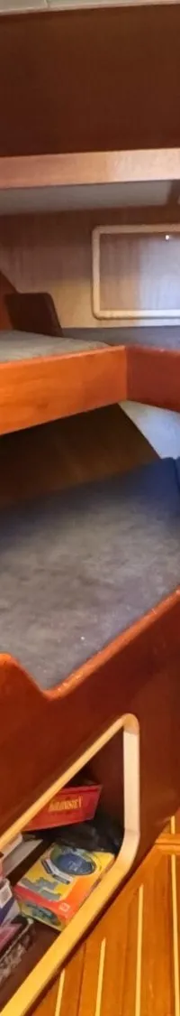 De foto toont een kajuit met houten wanden, twee stapelbedden met blauwe matrassen en een patrijspoort met een gordijn.