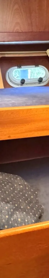 De foto toont een kajuit met houten wanden, twee patrijspoorten met gordijnen, en twee bedden met donkerblauwe kussens.