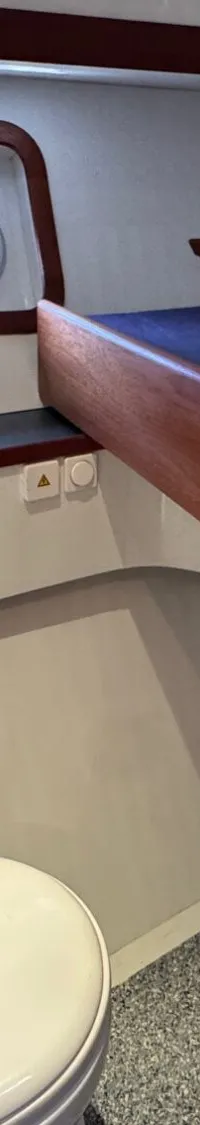 De foto toont een kajuit met een toilet, een bed met donkerblauw matras en een patrijspoort.