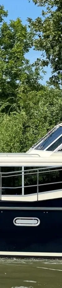 Een donkerblauwe motorboot met een crèmekleurige opbouw vaart op een waterweg met bomen op de achtergrond.