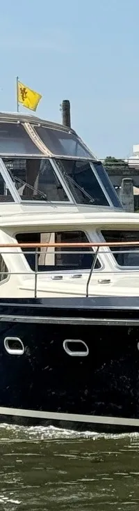 Een donkerblauwe motorboot met de naam "Twieberr" vaart op een waterweg met een brug en bomen op de achtergrond.