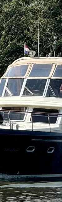 Een donkerblauwe motorboot met een lichte opbouw vaart op een waterweg met bomen op de achtergrond.