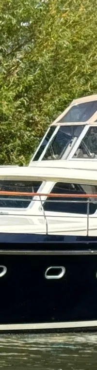 Een donkerblauwe motorboot met de naam "Twieberr" vaart op het water, met een beige kajuit en een Nederlandse vlag.