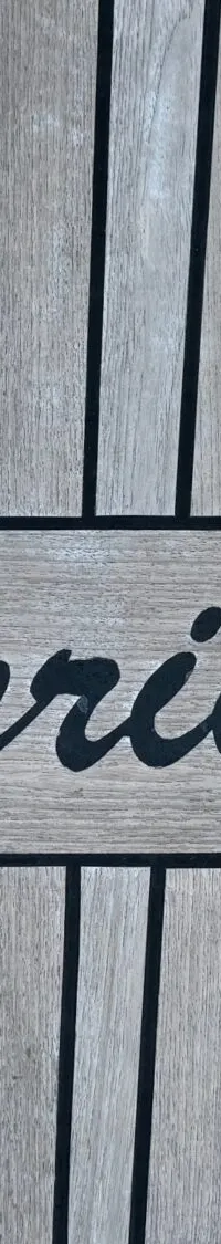 Een houten dek met een ingelegde rechthoekige plaat met afgeronde hoeken waarop in zwarte letters "Caprice" staat.