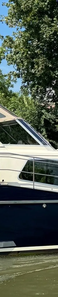 Een donkerblauwe motorboot met een crèmekleurige opbouw vaart op een waterweg met bomen op de achtergrond.