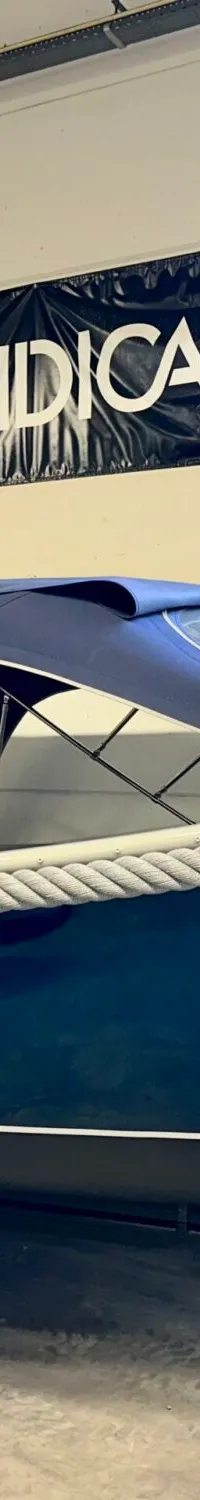 Een donkerblauwe boot met een touwrand en een blauwe kap staat op een kar in een loods. — Dutch Steel Dutch Steel Sloep 740
