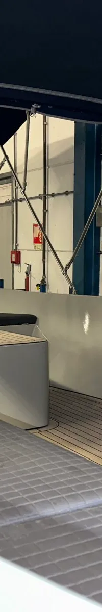 De foto toont het interieur van een boot met een donkerblauwe kap, grijze banken en een houten vloer.