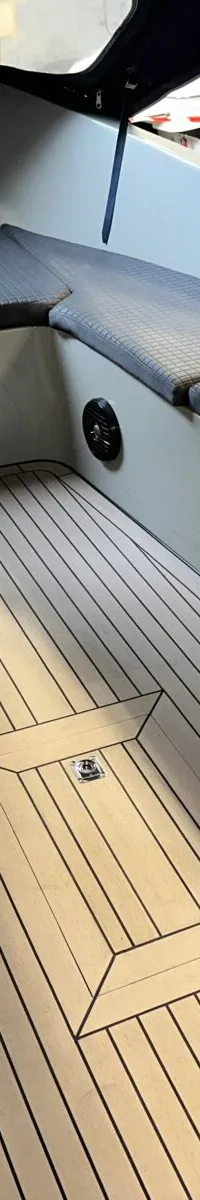 De foto toont het interieur van een boot met een U-vormige zitbank met donkere kussens en een lichte houten vloer.