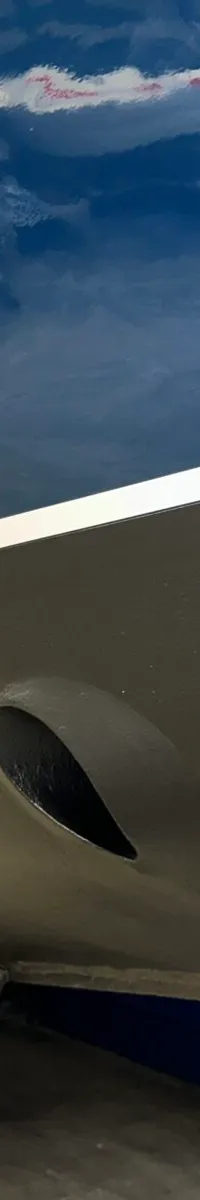 De onderkant van een blauwe boot met een grijze antifoulinglaag en een witte streep, staand op een trailer.