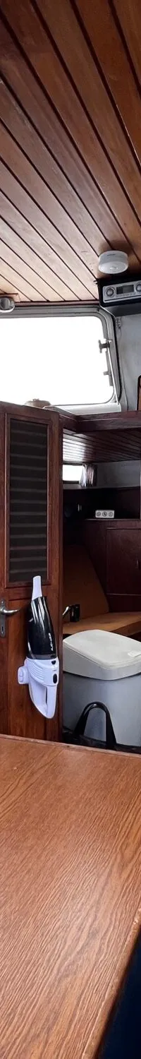 De foto toont het interieur van een boot met houten lambrisering, een stuurwiel, een tafel, een keukenblok en blauwe…