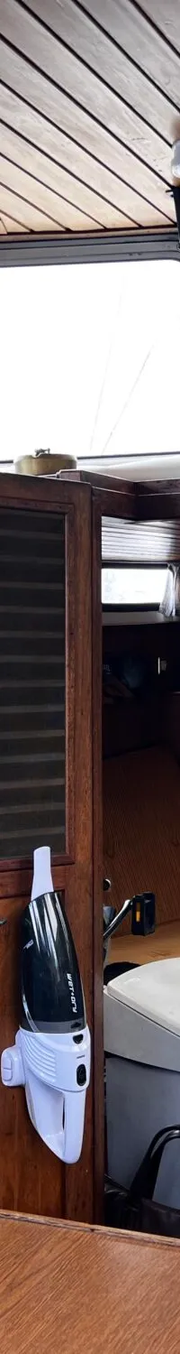 Een interieur van een boot met houten wanden en plafond, een stuurwiel, een koelkast en een gootsteen.