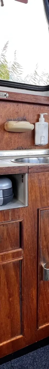 Een houten kombuis met een ingebouwde kookplaat, een gootsteen en opbergkasten, met uitzicht op riet.