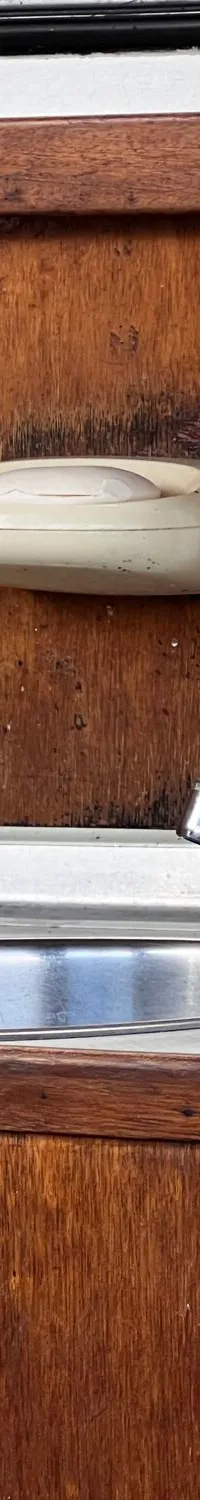 Een houten aanrecht met een metalen wasbak, een kraan, een zeepbakje, een zeepdispenser en een fles water.