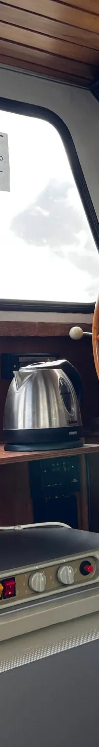 De foto toont het interieur van een boot met een stuurwiel, een koelkast, een waterkoker en een stofzuiger.
