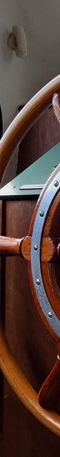 Een houten stuurwiel met metalen accenten, een waterkoker en een raam met uitzicht op bomen zijn zichtbaar.