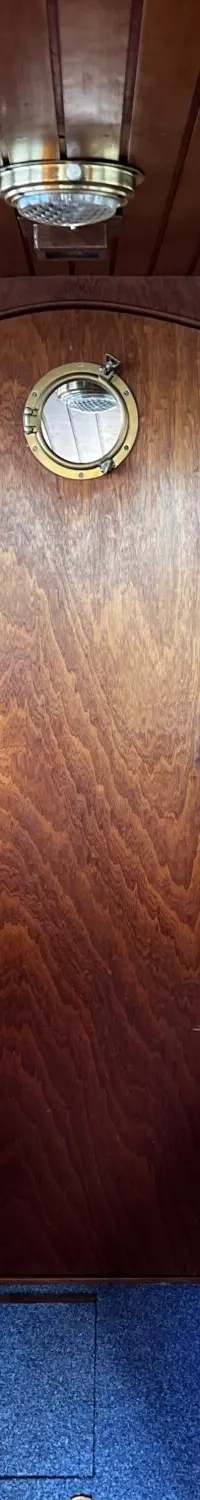 De foto toont het interieur van een boot met houten wanden en plafond, twee banken met gele kussens en een blauw tapijt.