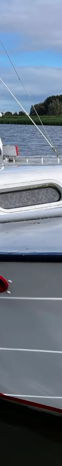 Een witte motorboot met de letters "JM" op het dak ligt aangemeerd aan een metalen steiger.