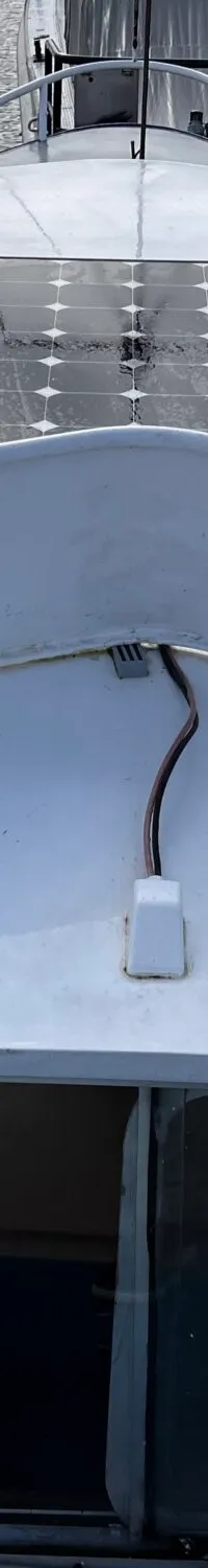Een witte boot met een zonnepaneel op het dak, een stuurwiel en een kajuit met ramen.