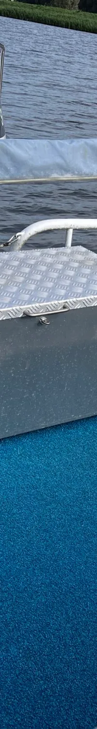 Een blauw tapijt bedekt de vloer van een boot met een stuurwiel en een metalen kist, naast een andere boot met "SK 342".