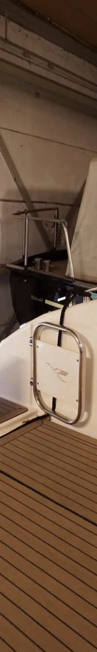 De foto toont de achtersteven van een boot met een bruin dek en witte zijwanden, met kussens en een opklapbare tafel.