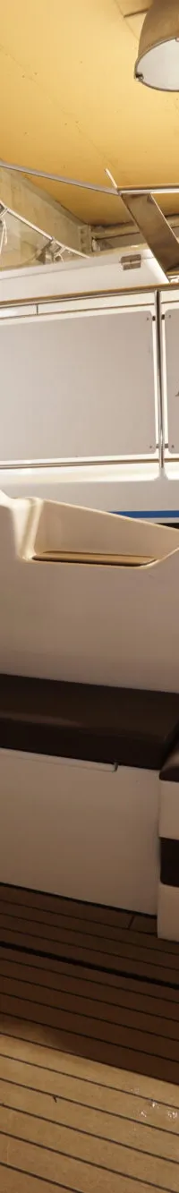 Een bootinterieur met een stuurstoel, een bankje, een tapijt en een koelkast, met een andere boot op de achtergrond.