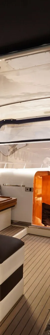 De foto toont het interieur van een boot met een zithoek, een stuurstand en een doorgang naar een kajuit.