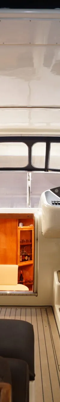 Een interieur van een boot met een houten tafel, donkere banken, een witte stuurstoel en een stuur.