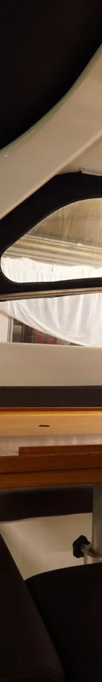 Een interieur van een boot met donkerbruine banken, een houten tafel en een wit plafond met ramen.