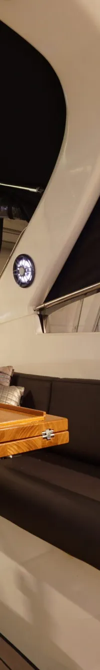Een interieur van een boot met een houten tafel, donkerbruine banken en kussens, en een zwart afdak.