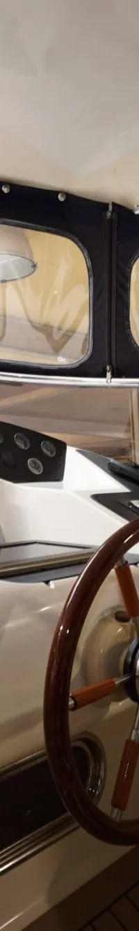 De foto toont het interieur van een boot met een stuurwiel, dashboard met meters en schakelaars, en een beige stoel.