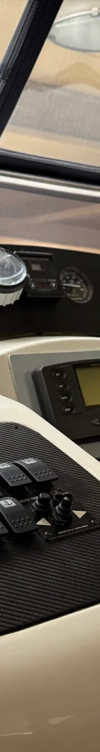 Een close-up van het dashboard van een boot met diverse meters, schakelaars, een scherm en een houten stuurwiel.