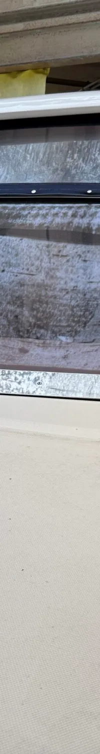 De foto toont de voorkant van een witte boot met een voorruit en een blauwe afdekking, binnen in een loods.