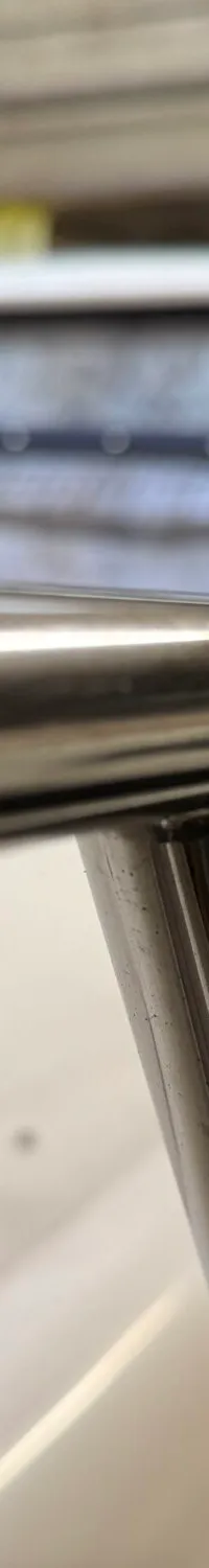 Een detailfoto van een glimmende metalen reling op een boot, met op de achtergrond een voorruit en een ander vaartuig.