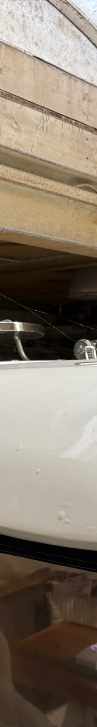 Een witte boot met een donkerblauwe kap en doorzichtige ramen staat onder een houten plafond met een dakraam.