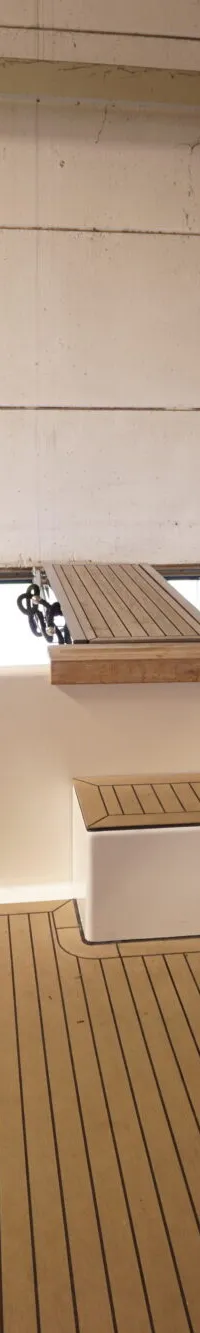 De foto toont het achterdek van een boot met bruine zitkussens, een houten vloer en een opklapbare gangway.
