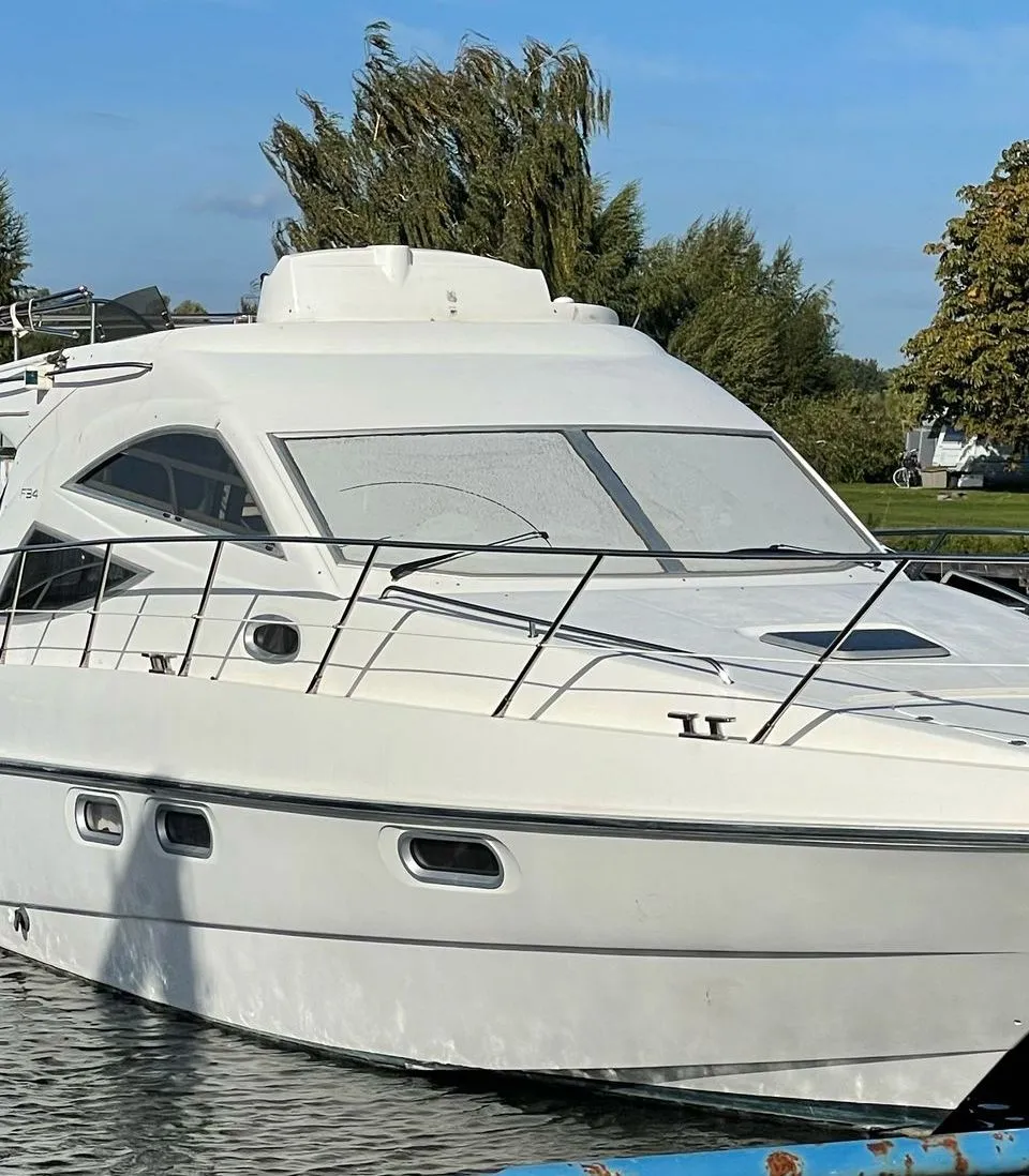 Een witte motorboot, met de naam "SEALINE" en "F34" zichtbaar, ligt aangemeerd in een haven. — Sealine Sealine F34 Flybridge