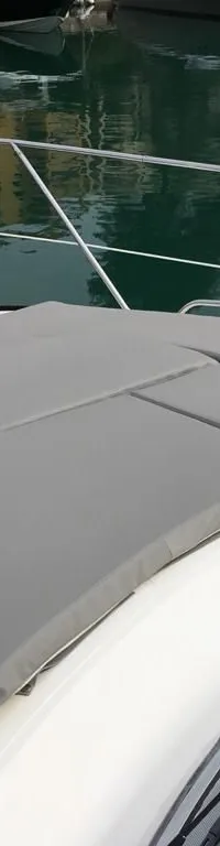 De foto toont het voordek van een boot met grijze kussens en een reling, liggend in een haven.
