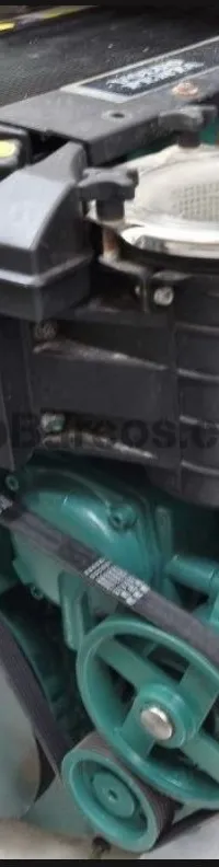 Een close-up van een scheepsmotor met riemen, poelies, filters en een zwart deksel.
