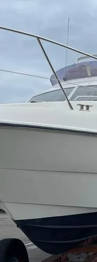 Een witte motorboot met blauwe onderkant staat op een trailer op een parkeerplaats, met andere boten op de achtergrond.