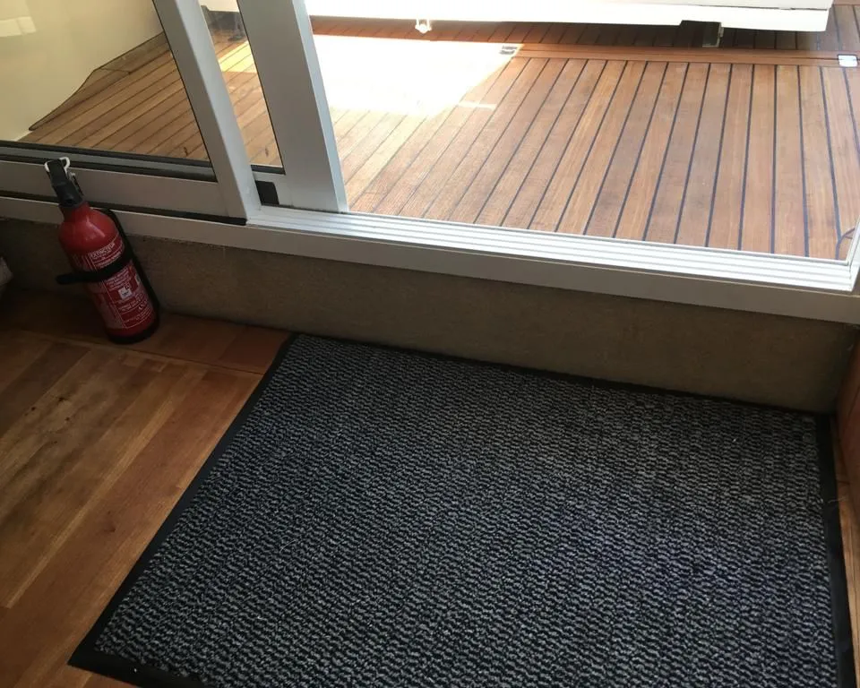 Een rode brandblusser staat op een houten vloer naast een grijs-zwart vloerkleed en een glazen schuifdeur.
