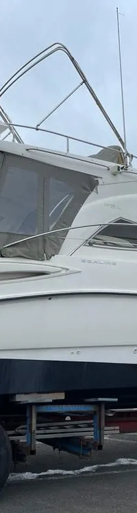 Een witte motorboot met donkerblauwe onderkant staat op een trailer op een geasfalteerd terrein onder een bewolkte lucht.