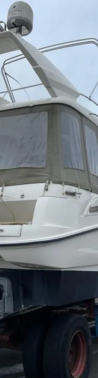 Een witte motorboot met twee buitenboordmotoren staat op een trailer op een parkeerplaats. — Sealine Sealine F34 Flybridge