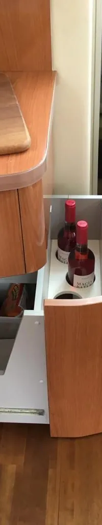 Een open lade met flessen wijn en glazen, naast een uitschuifbare lade met opbergvakken in een houten interieur.