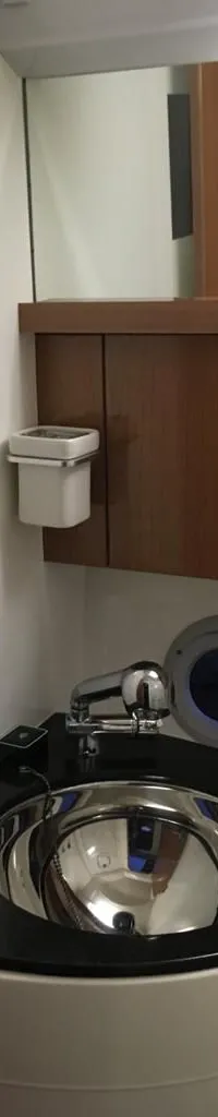 Een hoekige wastafel met een metalen kom en kraan, een spiegel en een patrijspoort zijn zichtbaar.