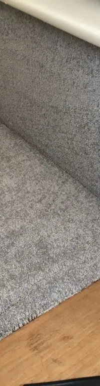 Een hoek van een interieur met grijze vloerbedekking op de vloer en wanden, en een houten vloer.