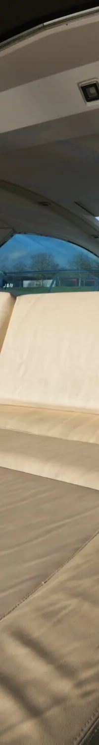 De foto toont een deel van een bootinterieur met beige kussens, een houten vloer en een stuurstand op de achtergrond.