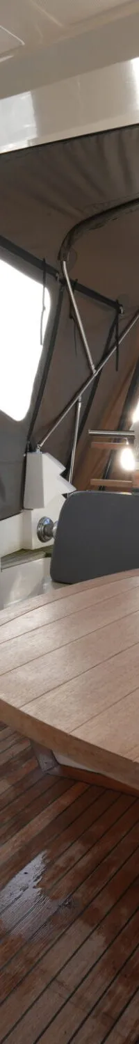 Een houten tafel met een snijplank en een glazen schaal staat op een teakhouten vloer in een bootinterieur met een kombuis.