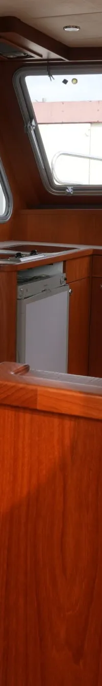 De foto toont het interieur van een boot met houten afwerking, ramen met blauwe gordijnen, een zitbank en een stuurconsole.