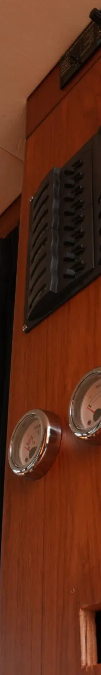 Een interieur van een boot met houten wanden, ramen met gordijnen, een plafond met verlichting en een bedieningspaneel met…